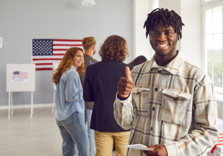 An African American man smiling and giving a thumbs up at an election polling location