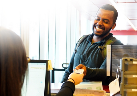 Man wearing a blue hoodie and backpack smiles as he is being handed a ticket.