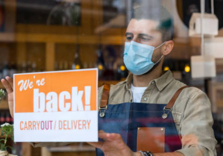 Shop owner holding up sign that reads, "We're back!"