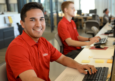 Image of two Mesa Community College students using computers and  wearing red polo shirts