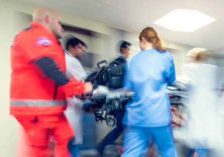 A blurred image of EMTs and medical professionals transport a patient in a hospital