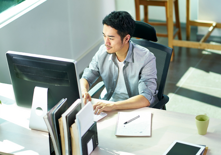 a man using a laptop sitting a brightly lit cubicle