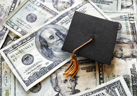 Image of money with a graduation cap laying on top of the money