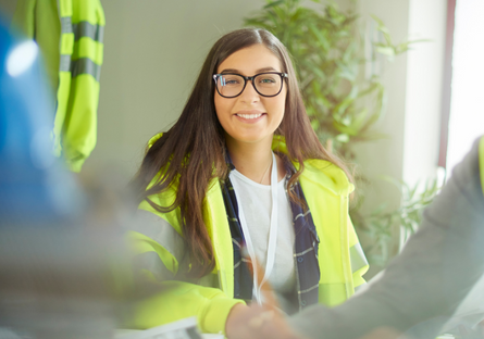 Image of a female construction worker how appears in focus with a male construction in the foreground 