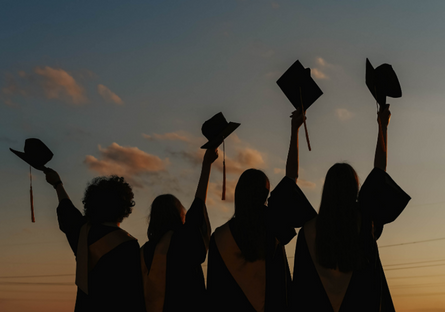 Image of four graduating students raising their caps in the air.