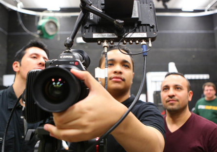 Image of three photo journalist student using a camera with a fourth person in the background