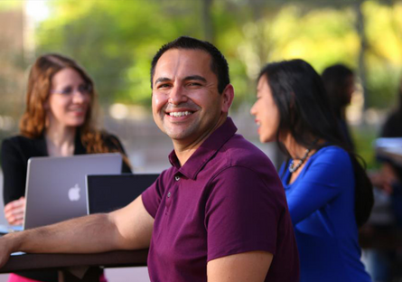 Image of a man wearing a maroon shirt smiling with students in the background