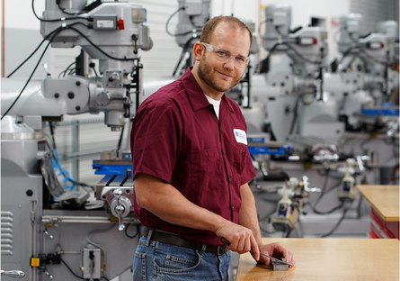 Image of a man wearing a maroon shirt smiling with machinery in the background