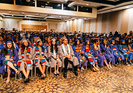 Room of students wearing cap and gowns during graduation ceremony.